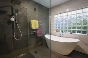 Glass-screened shower beside a freestanding bath and glass-block window.