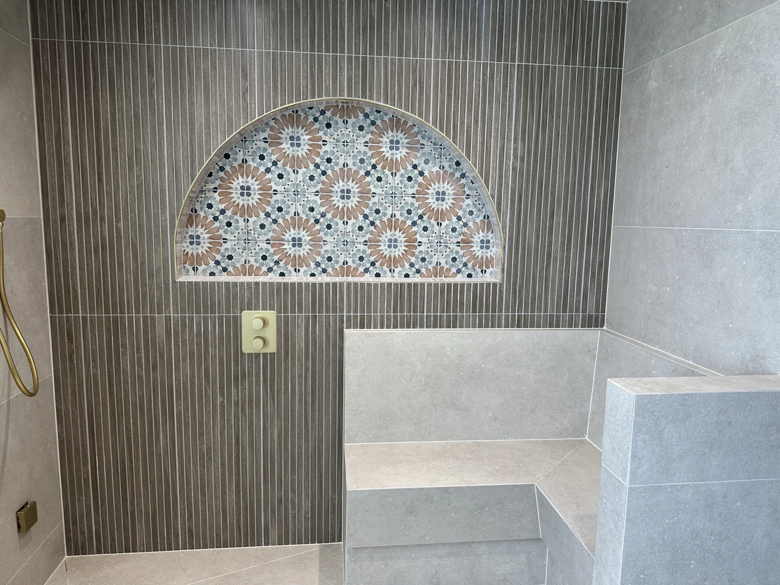 Built-in tiled shower seating beneath an arched patterned-tile wall recess.