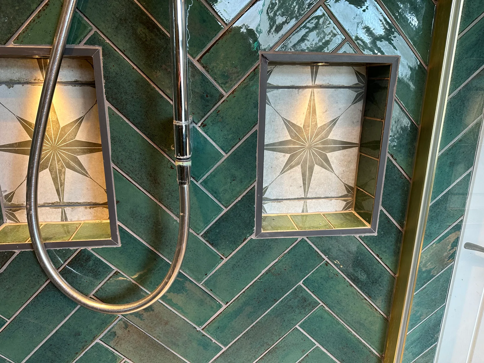 Two star-patterned storage niches within the teal herringbone shower wall in Bishops Cleeve.