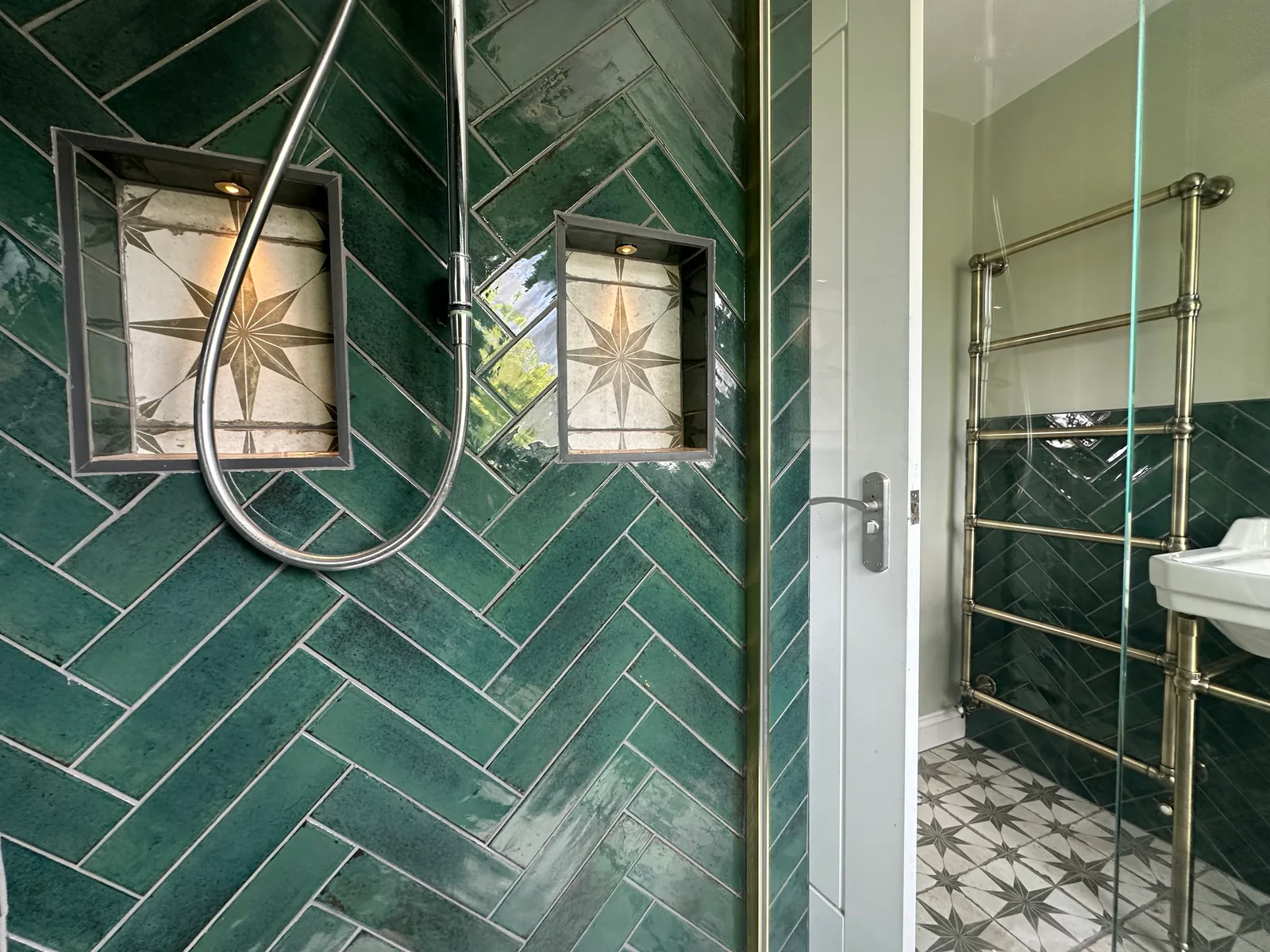 Glass shower screen and patterned storage niches within teal herringbone tiles in Bishops Cleeve.