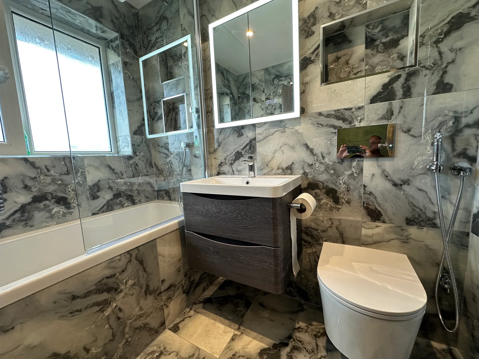 Finished Evesham bathroom with marble-effect tiling, bath, dark vanity unit and toilet.