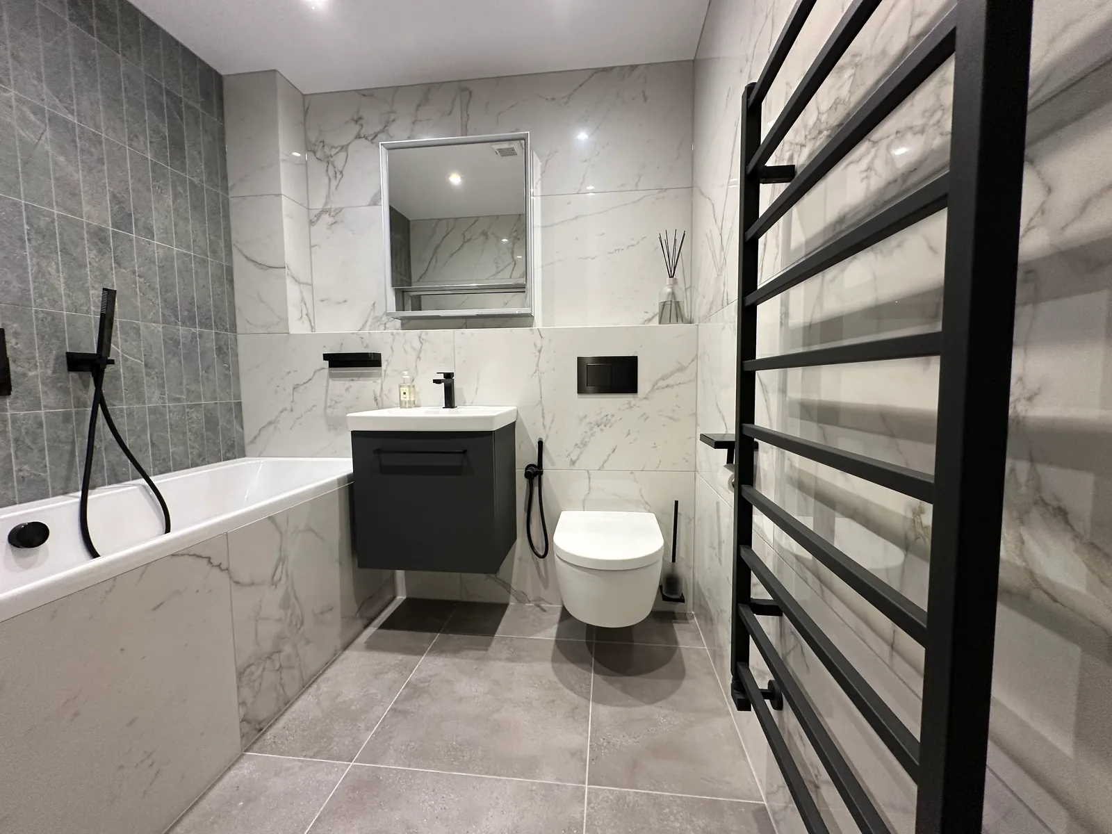 First Tuffley bathroom with a bath, dark vanity, wall-hung toilet and black towel rail.
