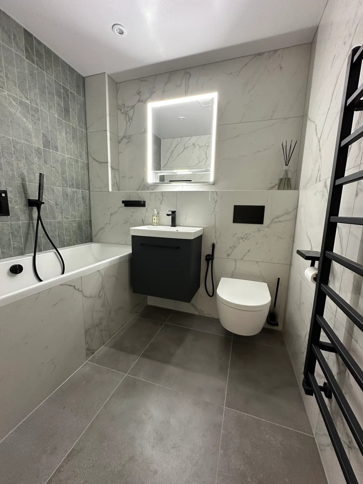 Two complete bathroom renovations in Tuffley, Gloucester 5 Illuminated Mirror Above A Dark Vanity Beside The Bath In The First Tuffley Bathroom.