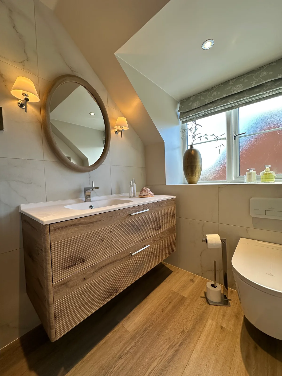 Twyning bathroom with wood-effect vanity, round mirror, toilet and glass shower screen